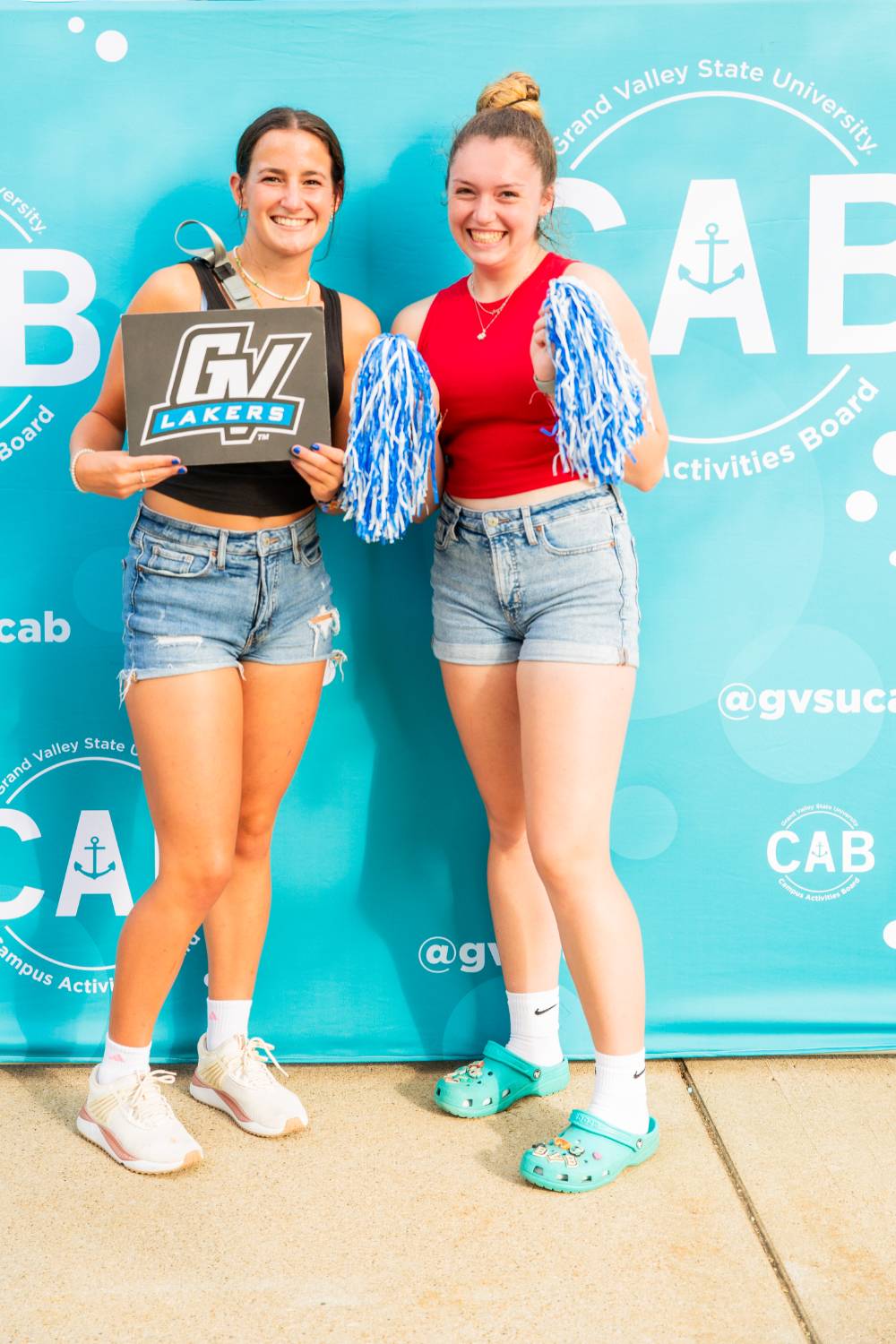 students posing in front of CAB backdrop at Laker Kickoff photo booth holding a GV sign and pom poms